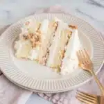 Banana Cream Cake – A Dreamy, Classic Dessert You’ll Crave 6 Slice of banana cream cake with whipped frosting and crumbled topping on a beige plate with gold fork.
